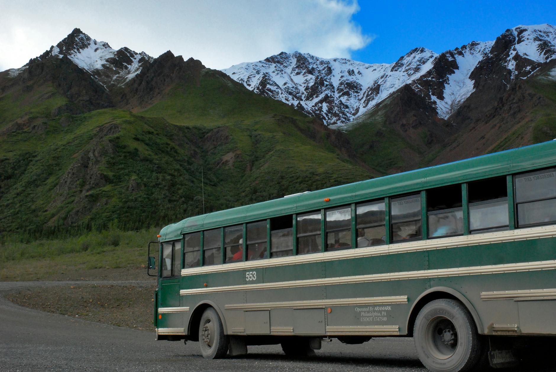 green and white buss on gray concrete top road across green mountains under cloudy sky